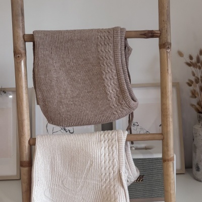 Dois coletes de malha castanho claro e creme pendurados numa escada de madeira natural