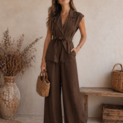 Conjunto feminino castanho com colete e calças largas, mala de mão em palha, sandálias castanhas, ambiente rústico