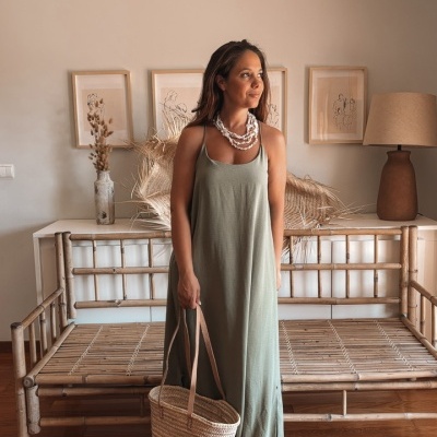 Mulher com vestido verde e saco de palha em espaço com banco de madeira e decoração neutra