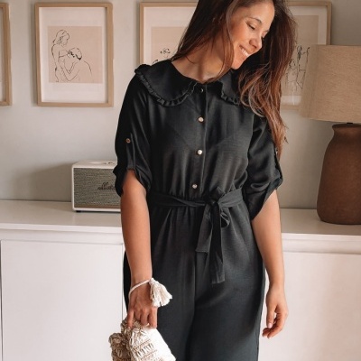Mulher com vestido preto e mala bege em quarto decorado.