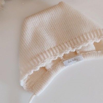 Gorro de bebé tricotado cru com etiqueta dori baby e plantas secas ao fundo