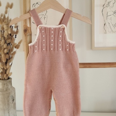Macacão de bebé em malha rosa com botões e bordados, pendurado em cabide de madeira