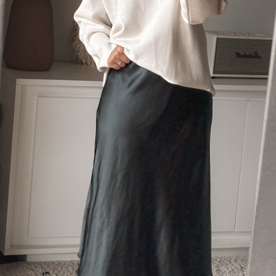 Mulher com camisola branca e saia preta em ambiente interior
