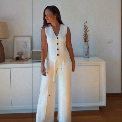 Mulher vestindo conjunto branco com colete e calças largas em sala minimalista.