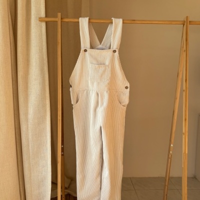 Macacão bege claro com riscas brancas pendurado numa estrutura de madeira