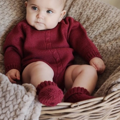 Bebé com camisola de malha vermelha sentado numa cesta com mantas bege felpudas