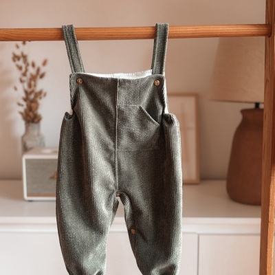 Peto infantil verde canelado com botões pendurado numa barra de madeira