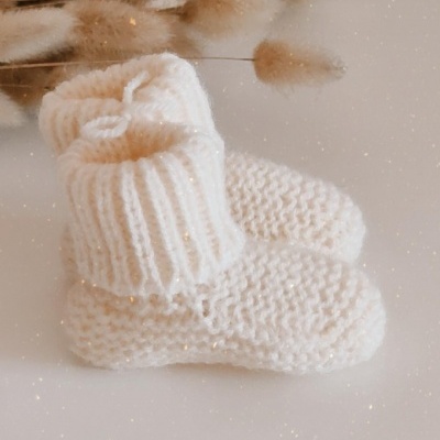 Botinhas de bebé brancas tricotadas com flores secas ao fundo