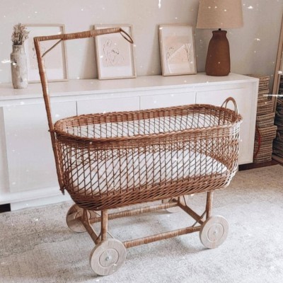 Berço de vime castanho claro com colchão branco em móvel branco e chão claro