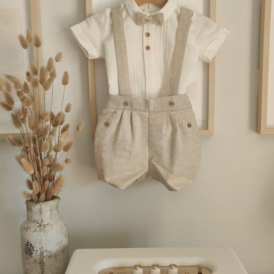 Conjunto de roupa infantil branco e bege pendurado na parede com decoração