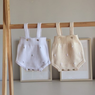 Dois macacões de bebé em malha branco e bege pendurados num varão de madeira