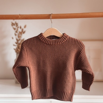 Camisola castanha de malha grossa numa cabide de madeira.