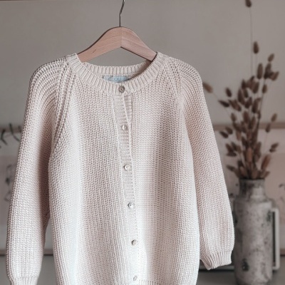 Cardigã de malha grossa bege pendurado num cabide de madeira