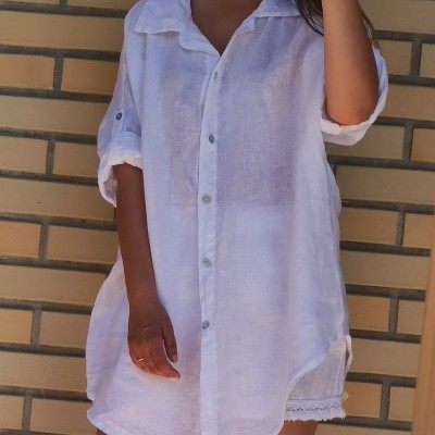 Camisa branca de linho com botões e mangas arregaçadas em fundo de parede de tijolos