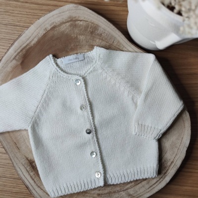 Camisola de bebé branca com botões prateados sobre base bege e madeira clara
