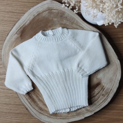 Camisola branca de malha com mangas compridas e gola alta sobre apoio de madeira e planta seca