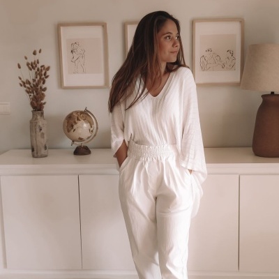 Mulher com roupa branca casual, blusa de manga longa, calças e sapatilhas, em ambiente interior com decoração neutra.