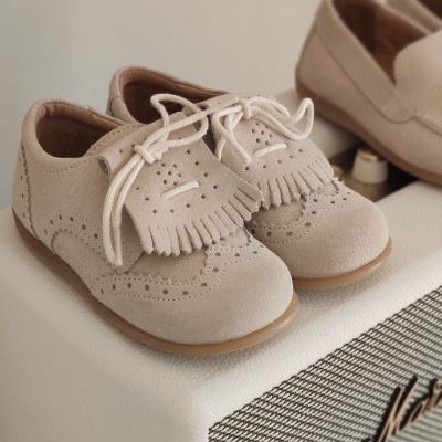 Sapatos de bebé em camurça bege clara com detalhes perfurados e franjas sobre coluna de som Marshall branca