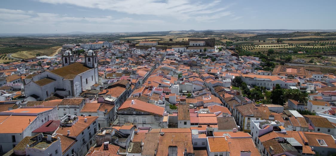 Festas do Povo de Campo Maior 2026 - Pack Hotel + Entrada Vista aérea de cidade com telhados laranja e igreja com torres