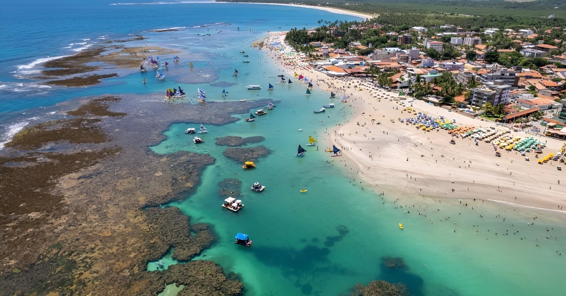 Brasil - Recife e Porto de Galinhas - Paraíso Nordestino (7 Noites - TI) Praia com mar azul, veleiros coloridos, areia clara e espreguiçadeiras coloridas.
