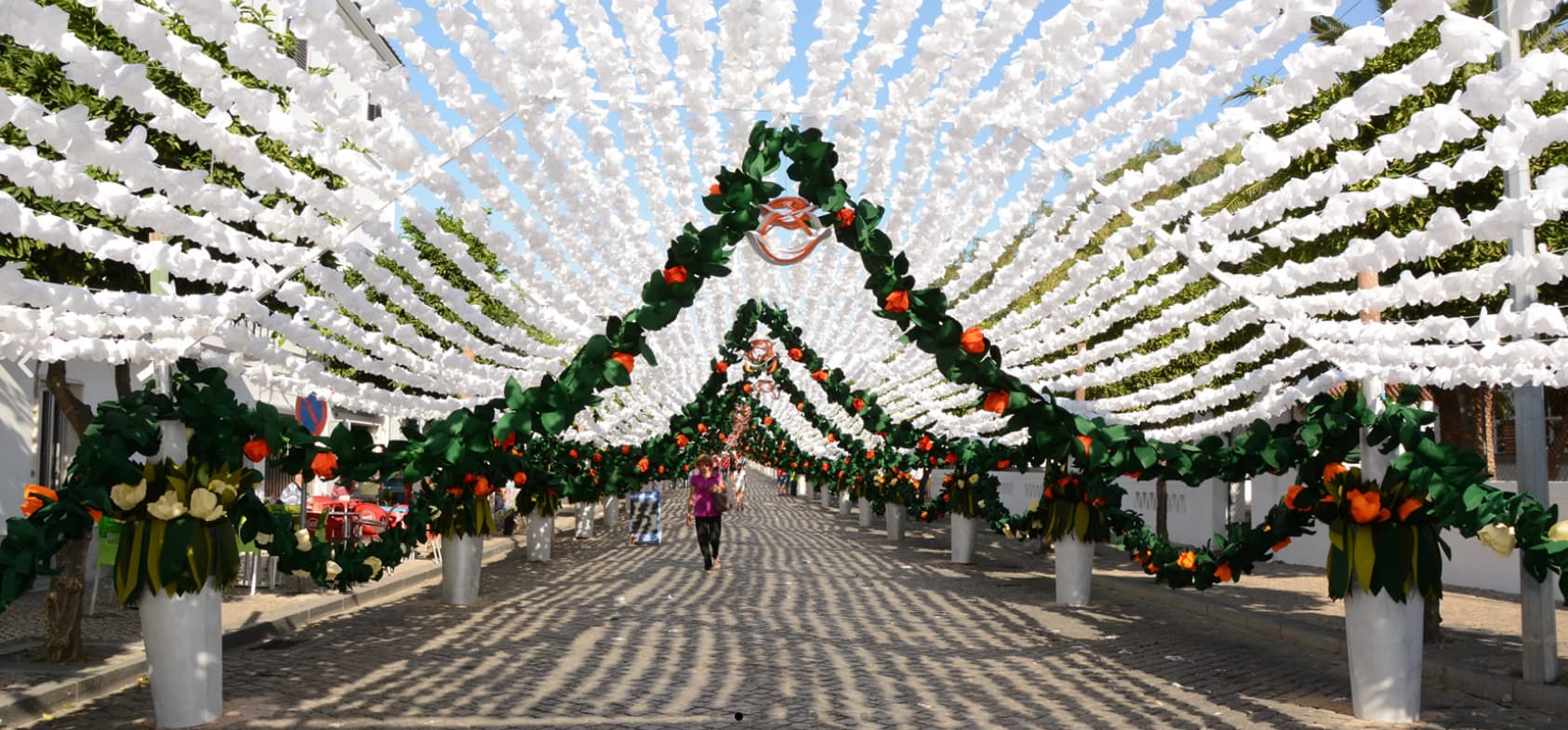 Festas do Povo de Campo Maior 2026 - Pack Hotel + Entrada Decoração exterior com flores artificiais verdes, laranja e brancas suspensas numa rua