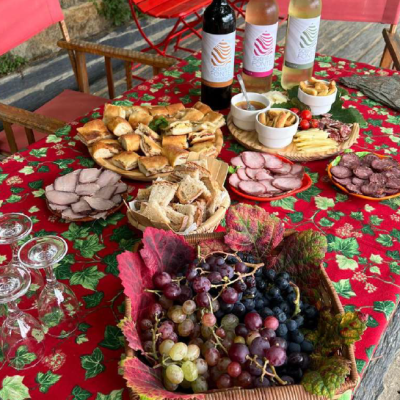 Mesa exterior com comida, vinho e cadeiras coloridas junto a parede de pedra