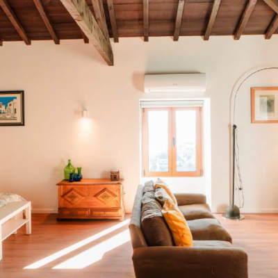 Quarto e sala com tecto em madeira, cama branca e sofá castanho