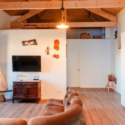 Sala com lareira metálica, sofá castanho, móvel de madeira com TV e cozinha branca com bancada de madeira.