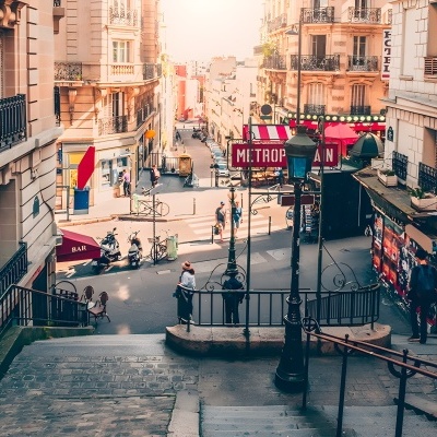 Escadaria em rua com edifícios clássicos, varandas, sinal METROPOLITAIN e toldo BAR