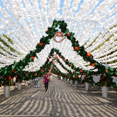 Decoração exterior com flores artificiais verdes, laranja e brancas suspensas numa rua