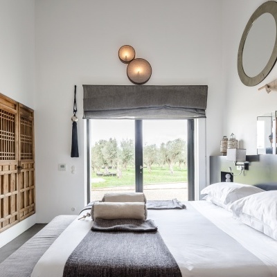 Quarto minimalista com cama branca, mantas cinzentas e janela ampla para jardim