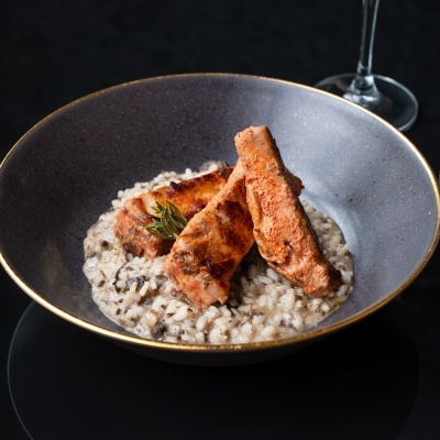 Prato com risoto de cogumelos e salmão grelhado sobre mesa preta com talheres e copos