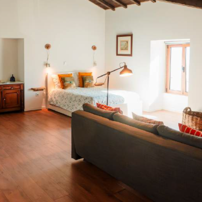 quarto espaçoso com cama de casal, sofá cinzento, mesa de madeira esculpida, TV e janela de madeira