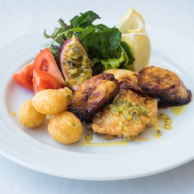 Prato de peixe frito com maracujá, batatas, banana frita, tomate, salada e limão.