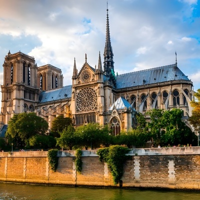 Catedral gótica em pedra clara com rosácea e torres junto a um rio e árvores