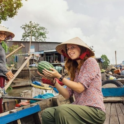 Duas mulheres de chapéus cónicos num barco de madeira seguram uma melancia num mercado fluvial