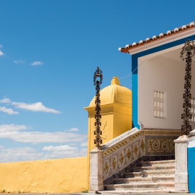 Escadaria exterior decorada com azulejos e parede amarela junto a edifício branco e azul sob céu azul