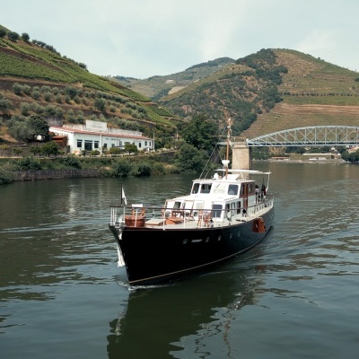 Barco de recreio em rio com colinas e Ponte de Ferro ao fundo