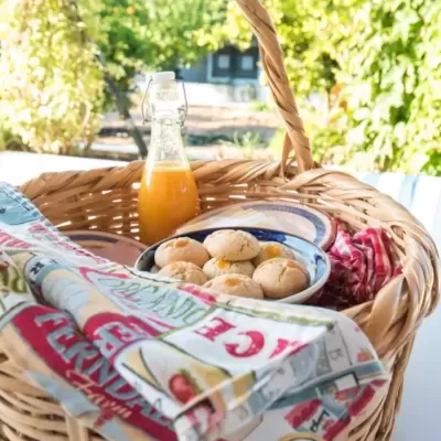 Cesto de verga com bolachas, frasco de sumo e panos coloridos numa mesa branca ao ar livre