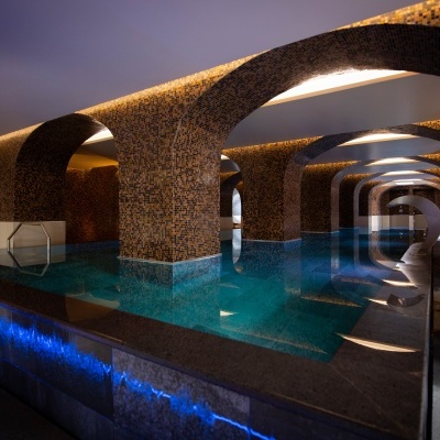 Piscina interior com colunas revestidas a azulejos e luzes LED azuis na borda.