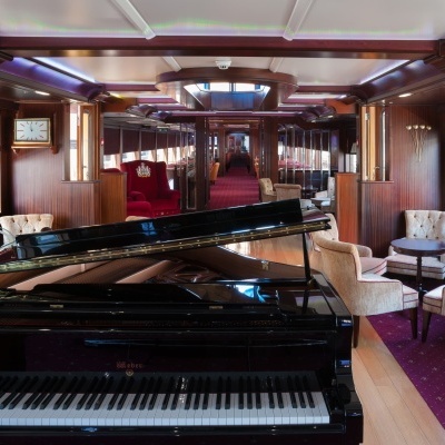 Piano de cauda preto num salão com cadeiras estofadas e decoração clássica de madeira