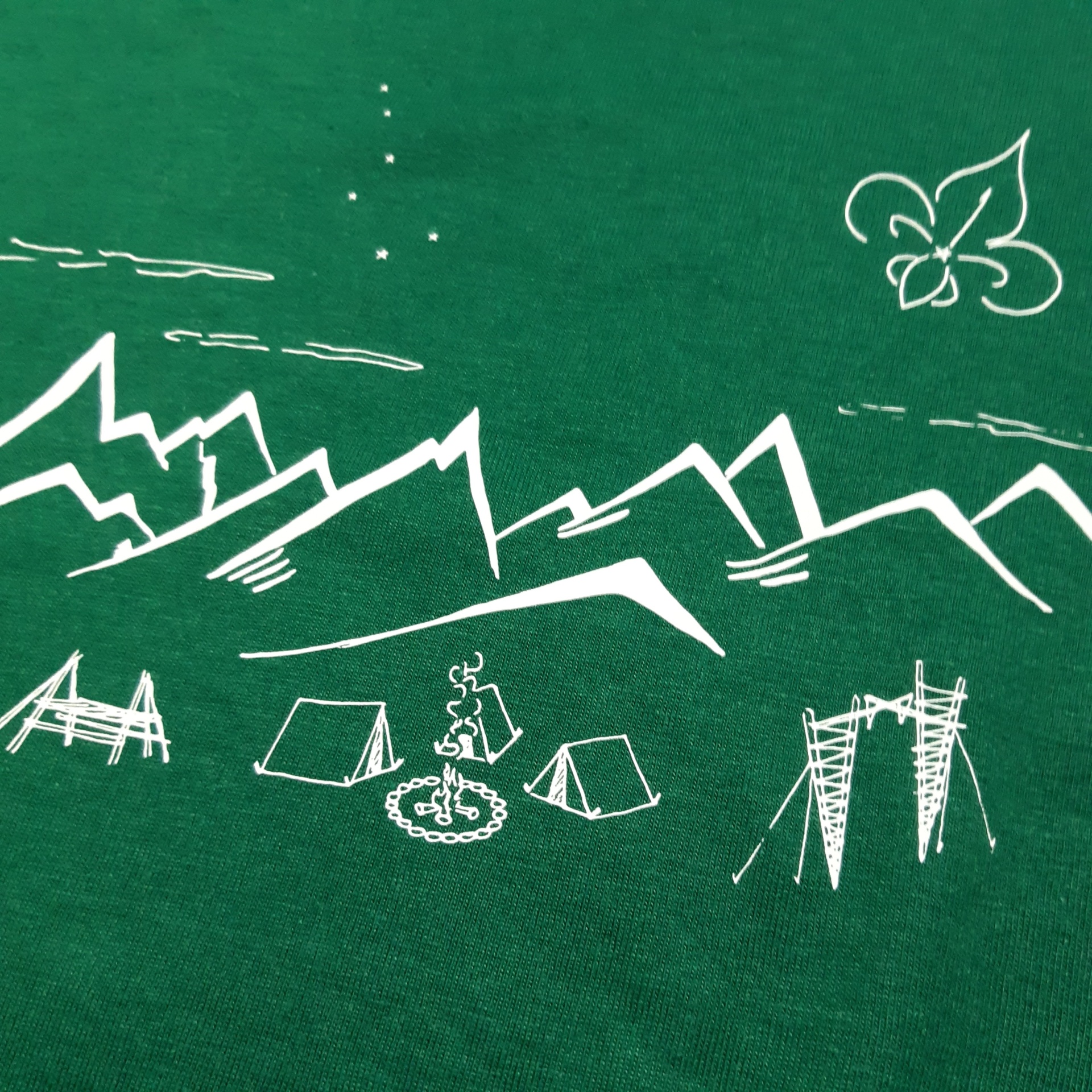 Tecido verde com desenho branco de montanhas, tendas, fogueira e flor-de-lis