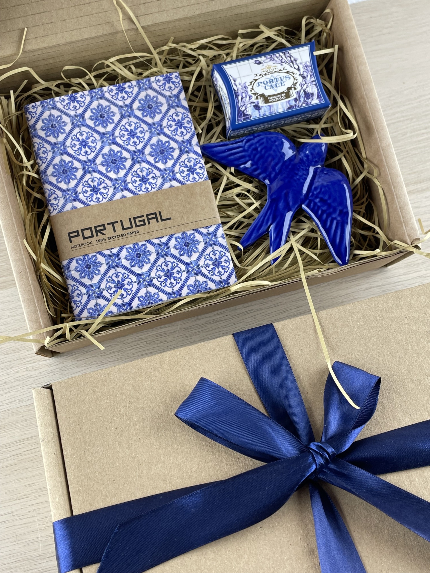 Gift box with notebook, soap, and blue ceramic bird on straw packing
