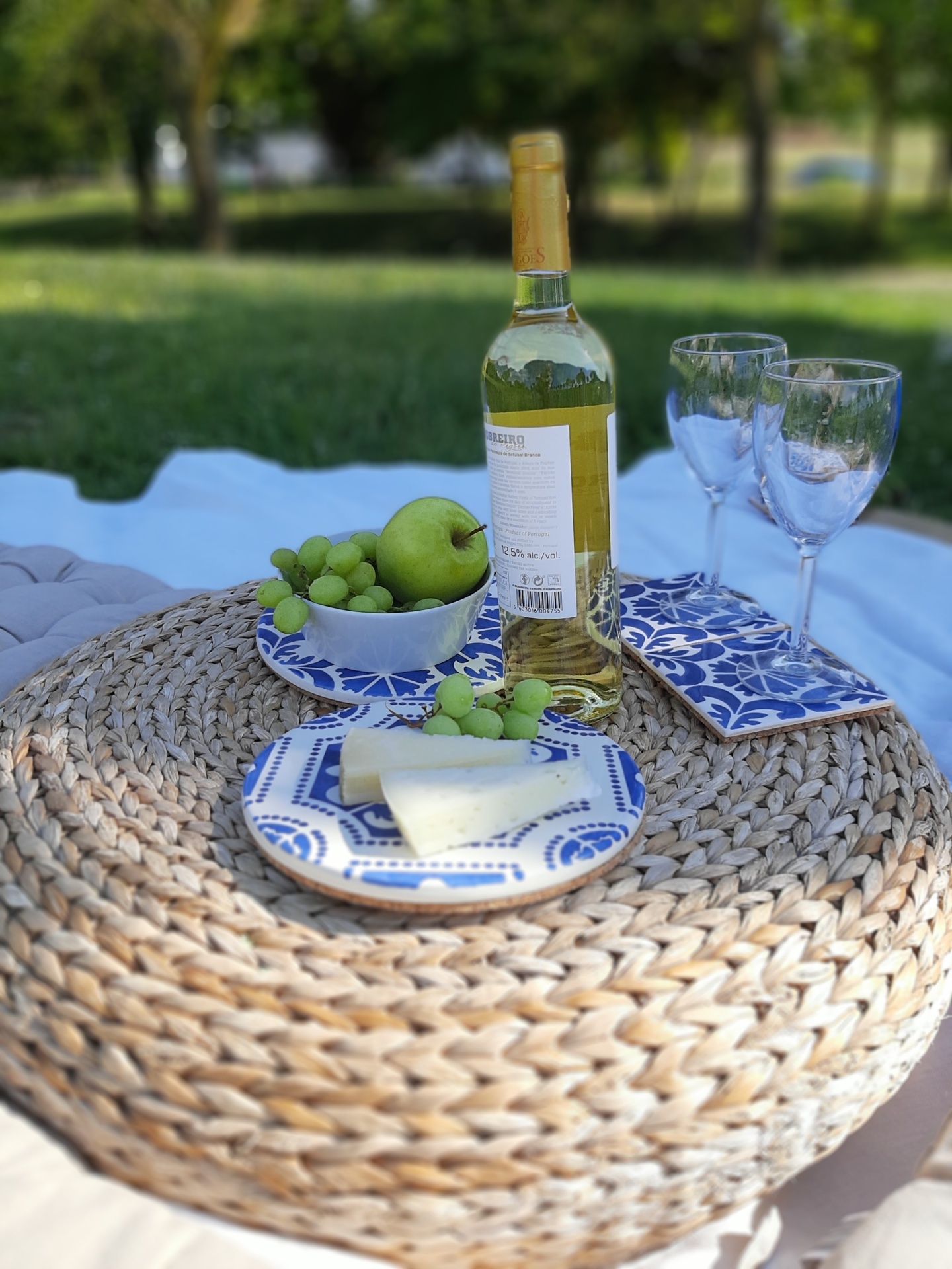 Picnic setup with wine bottle, glasses, fruits, cheese on woven mat