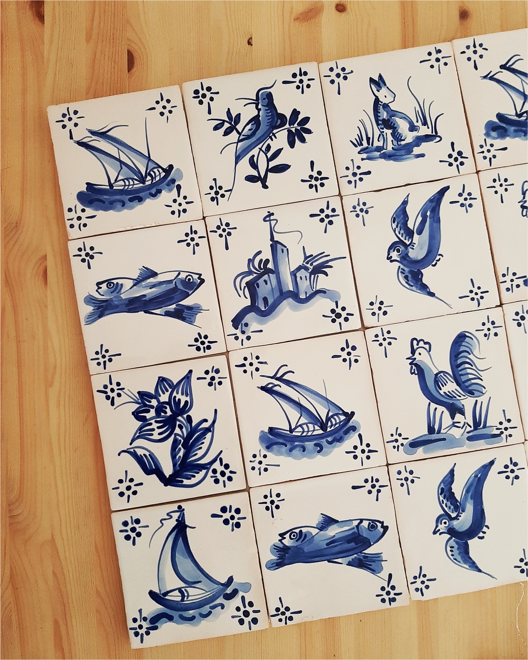 Hand-painted blue and white ceramic tiles with various nature and nautical designs on wood