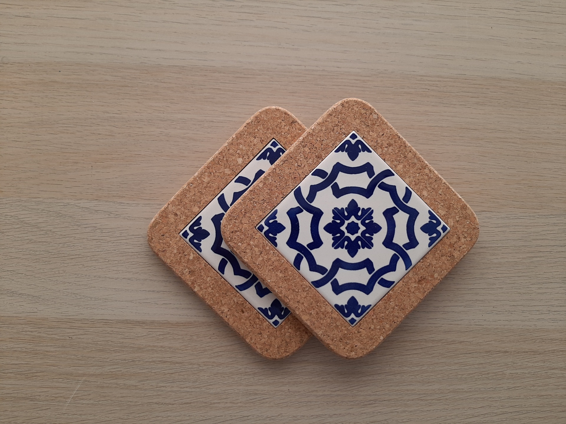 Two cork coasters with blue and white patterned ceramic centers on a wooden surface