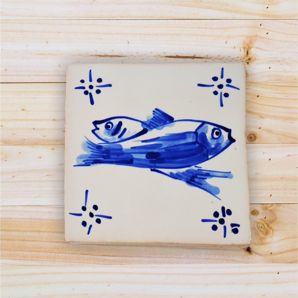 Ceramic tile with blue fish painting and corner motifs on wood surface