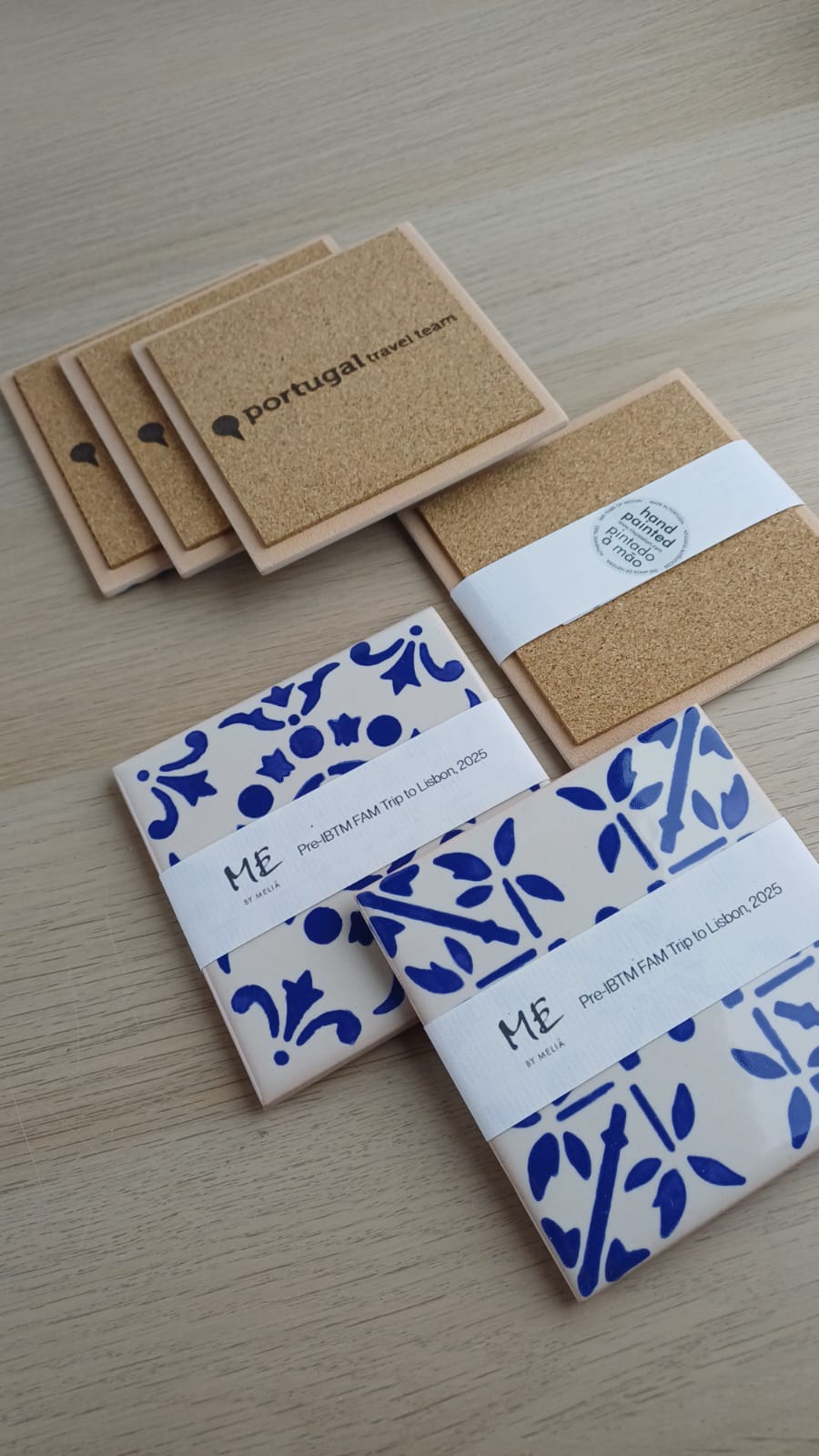 Square cork and ceramic coasters with printed text and blue patterns on a light wooden table