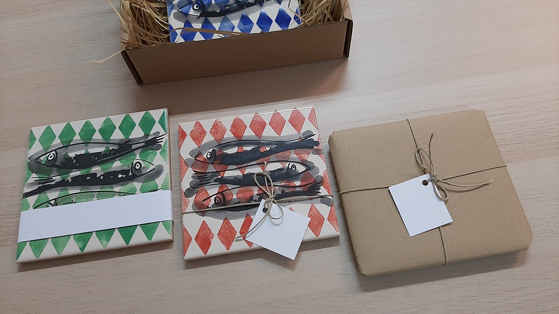 Three ceramic tiles with fish and diamond patterns and one wrapped in brown paper with twine on wooden surface