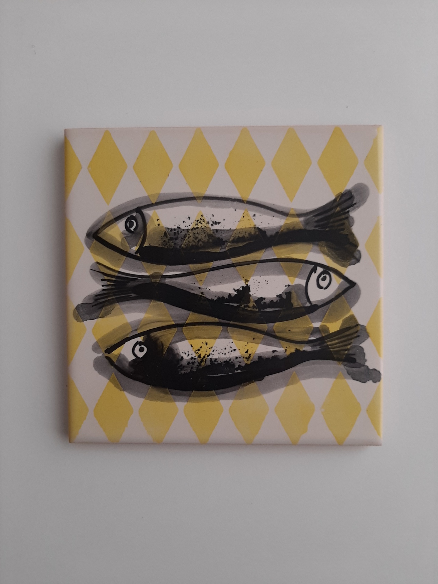 Azulejo com três peixes sobre padrão de losangos amarelos